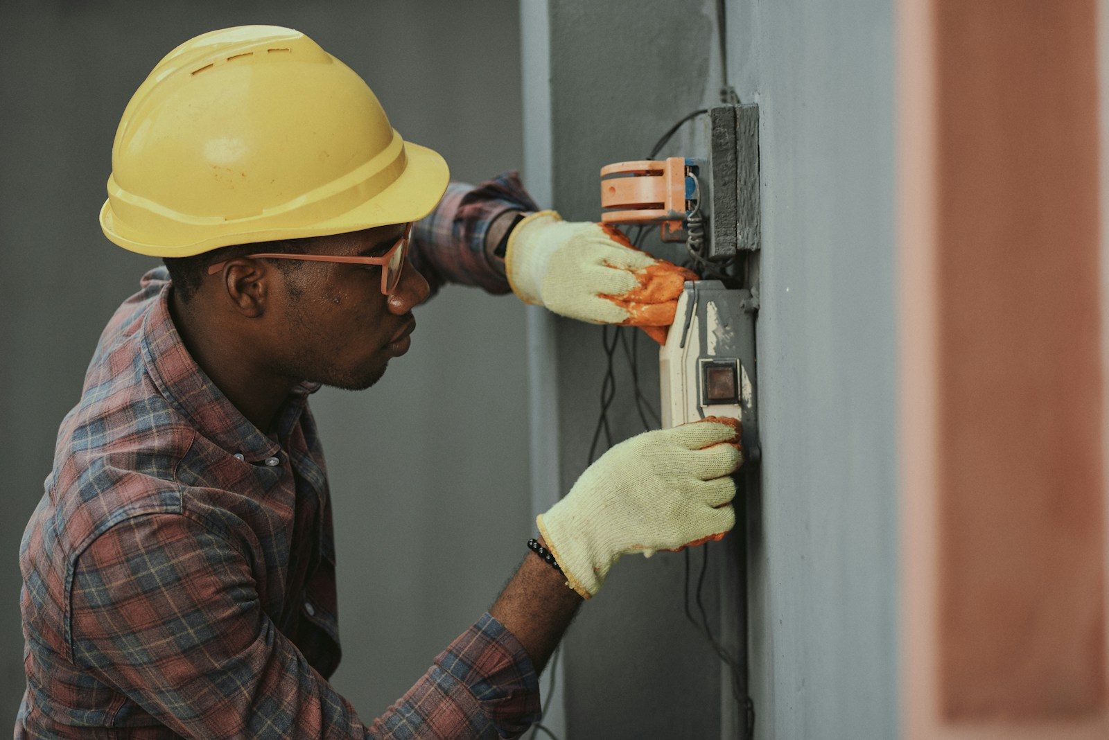 Electrician in a yellow hard hat wiring a wall switch box